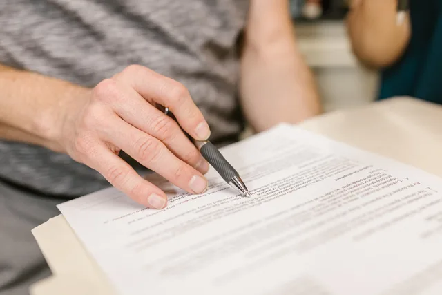 Close-up of a person's hand signing an important legal document with a pen indoors. Lejevilkår i erhvervslejemål: fra depositum til fraflytning